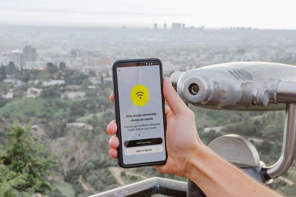Persona sosteniendo un smartphone con app de conectividad de datos móviles y skyline urbano de fondo
